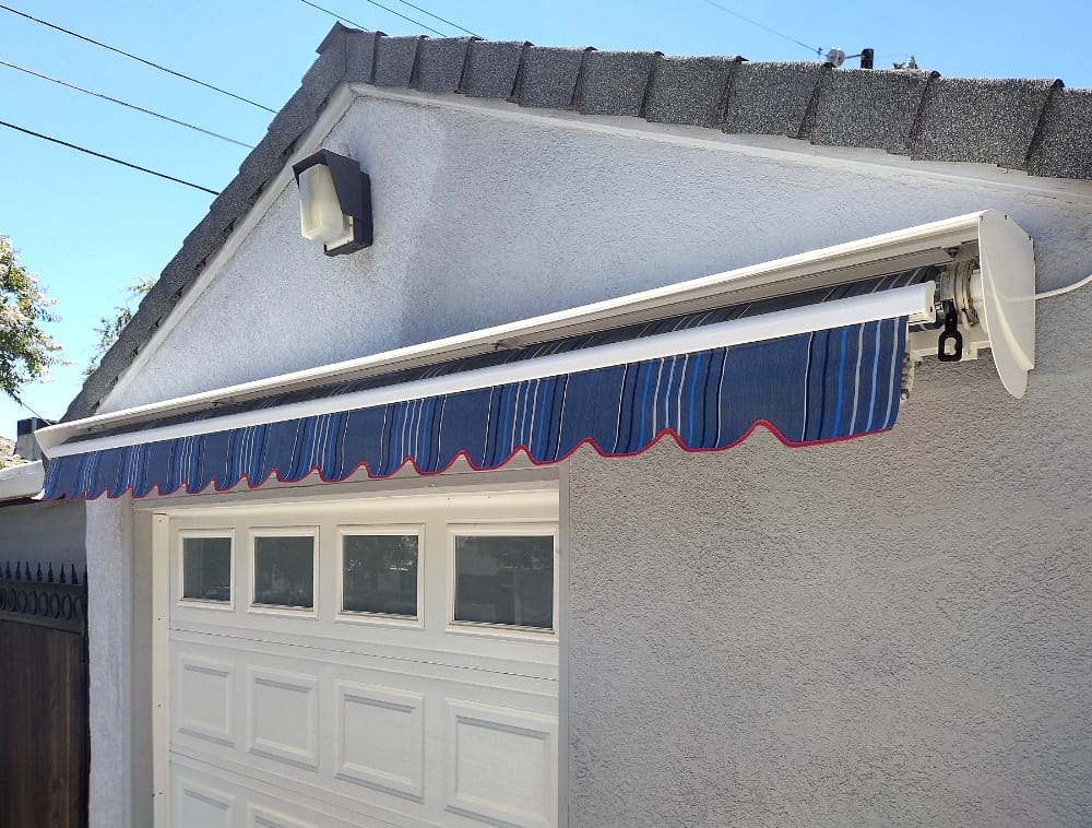 A residential garage featuring a white garage door and a retractable blue striped awning above it.