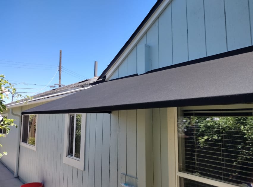 A black awning is installed on the side of a residential home, serving as a stylish element while providing shade and shelter.